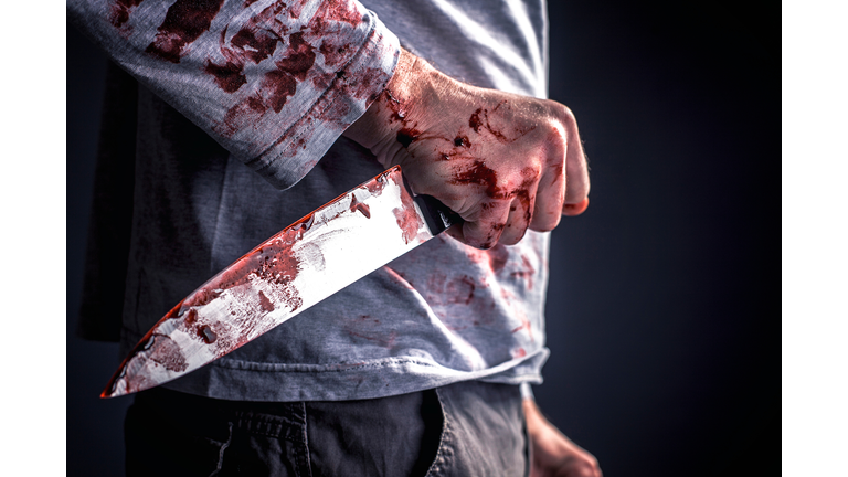 Midsection Of Murderer Holding Blooded Knife Against Black Background