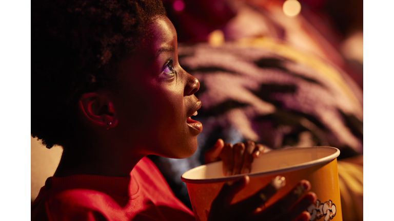 Shocked girl with popcorn watching thriller movie in cinema hall at theater