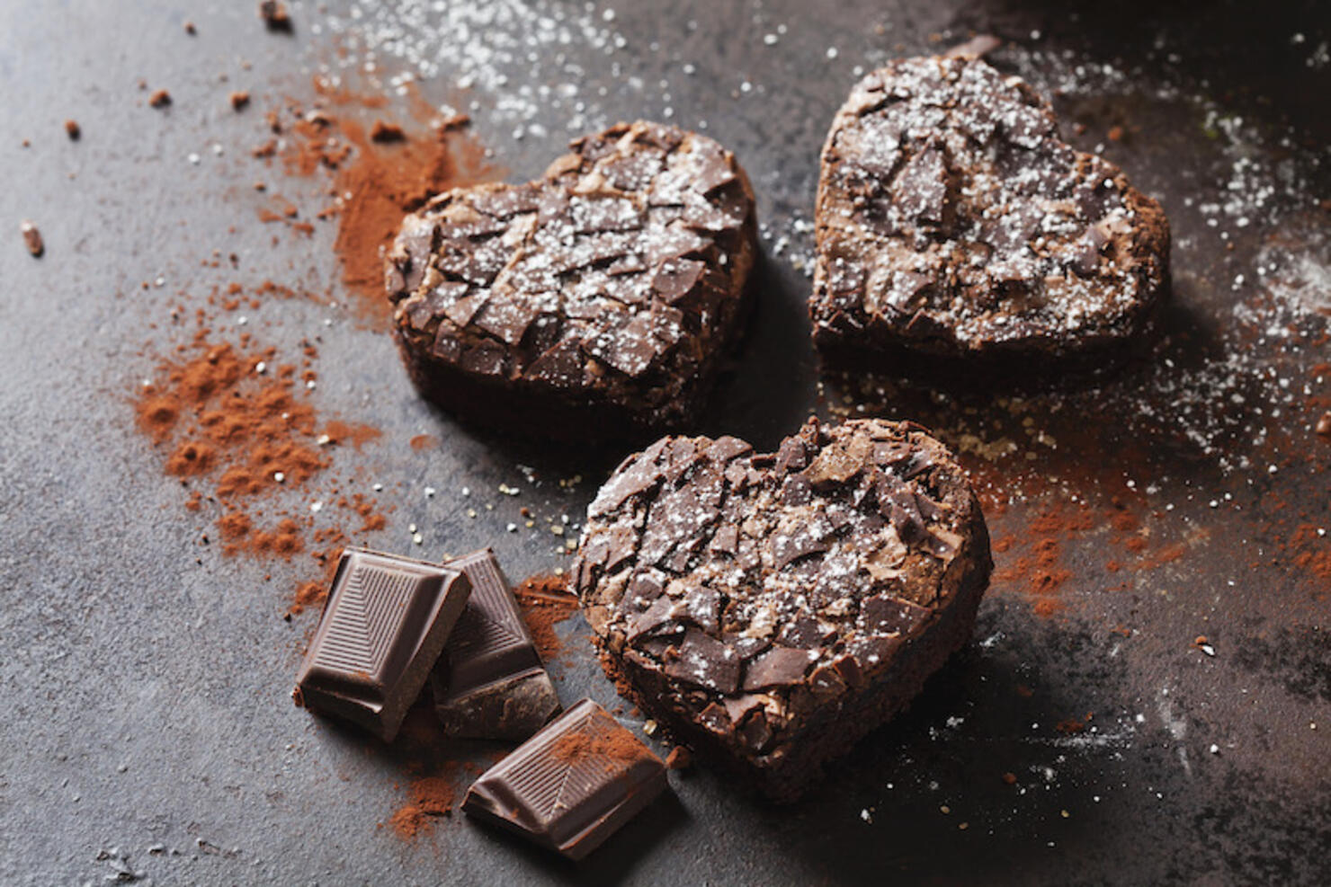 Three heart-shaped brownies and chocolate on metal