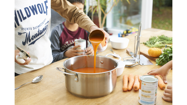 Cropped shot of boy pouring tin of tomato soup into saucepan