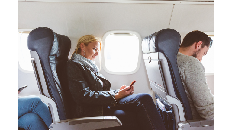 Mature woman traveling by airplane with mobile phone