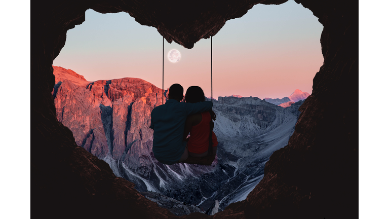Couple on swing contemplating the mountains in a romantic view with heart shape.