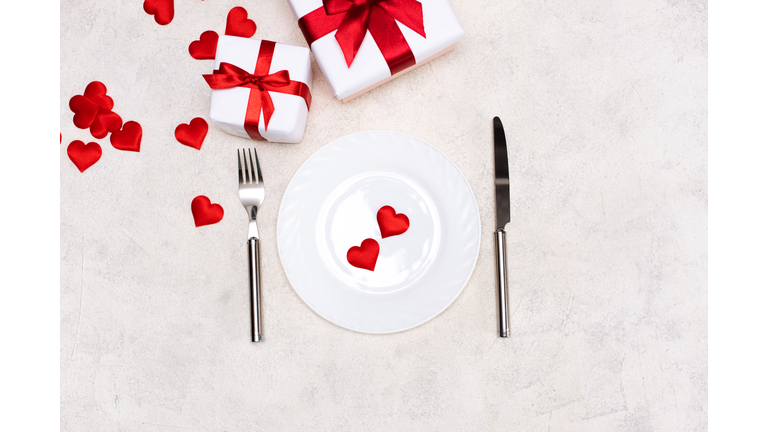 Valentine's day table setting with plate, fork, knife, gift box and red heart, on red tablecloth background top view copy space