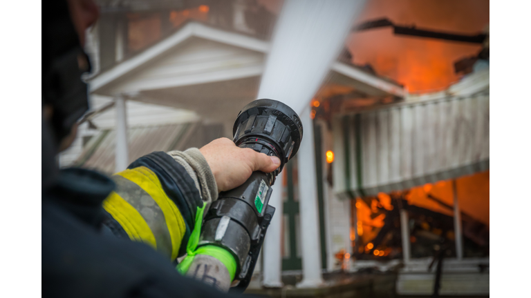Close-Up Of A Firefighter Spraying Burning House With Hose
