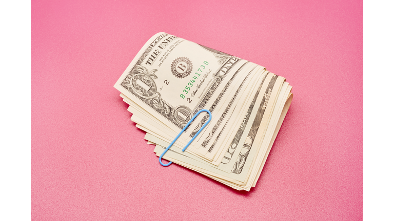 Directly above shot of a bundle of American Dollar bank notes with blue paper clip on pink background