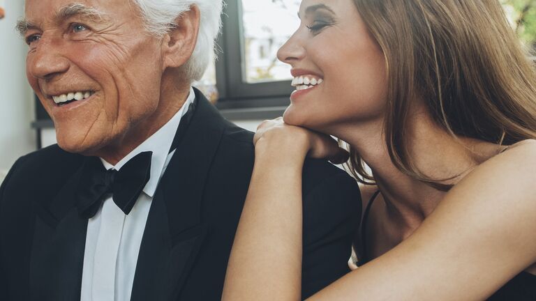 Smiling young woman with elegant senior man on couch