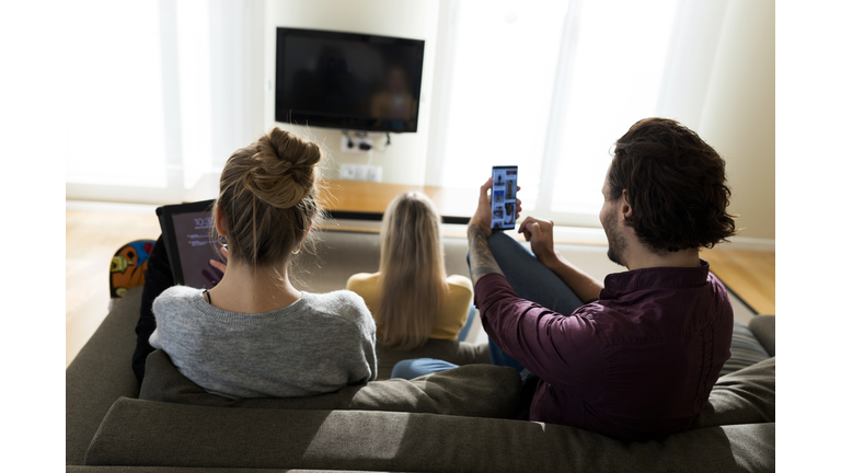 Friends sitting on couch in livingroom, using digital devices