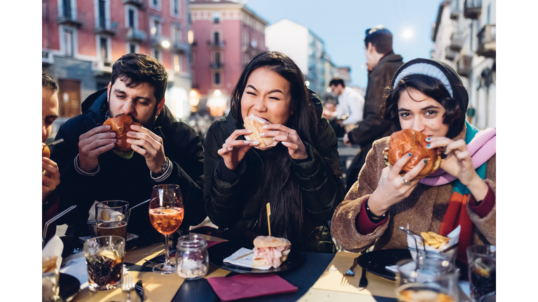 Friends enjoying burger at outdoor cafe, Milan, Italy