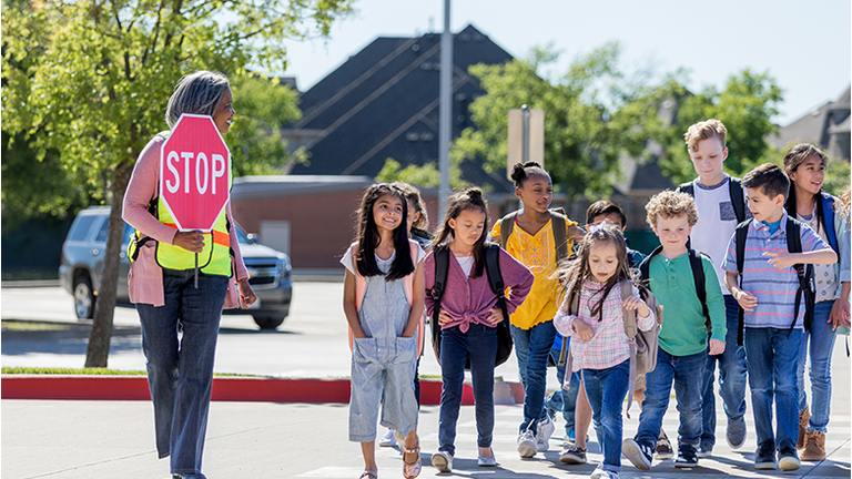 Female crossing guard leads children safely across street