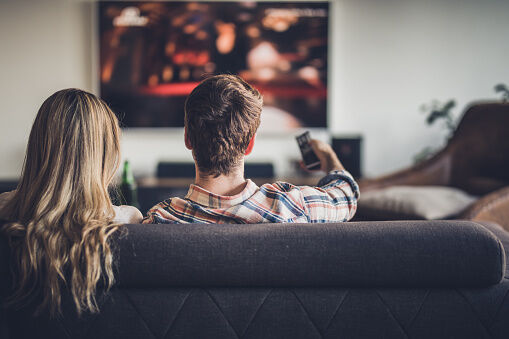 Rear view of a couple watching TV while relaxing on the sofa at home.