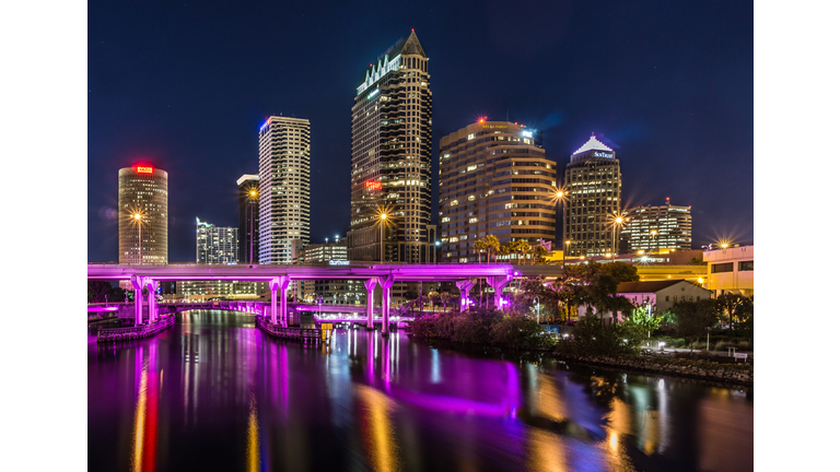 Illuminated Purple Bridge Over River In City Against Sky