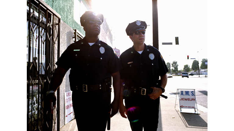 Two policemen wearing sungalsses, walking down sidewalk