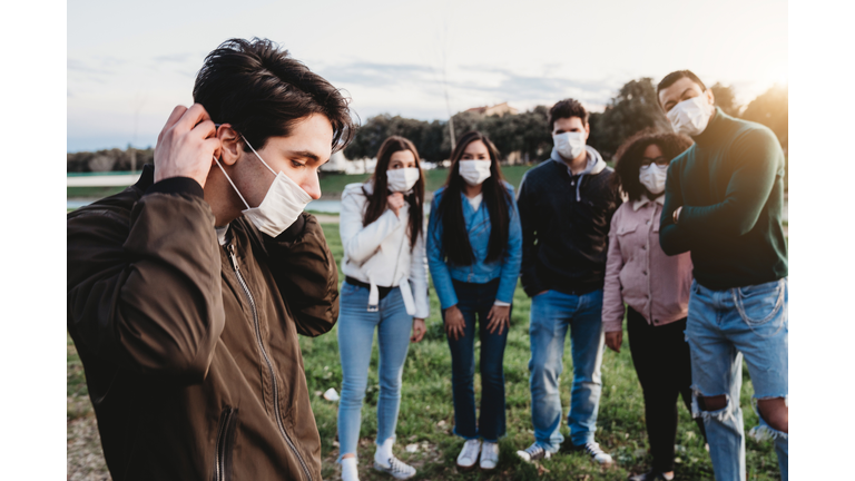 Young adult man wearing a pollution mask to protect himself from viruses. His friends are in the background.