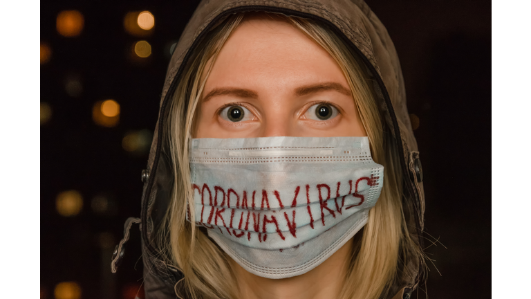 blonde girl in a hood with a medical mask on her face with the inscription coronavirus in the dark. Concept of health care, medicine