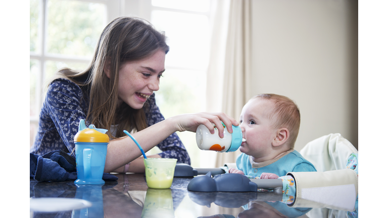 Girl feeding baby brother at table