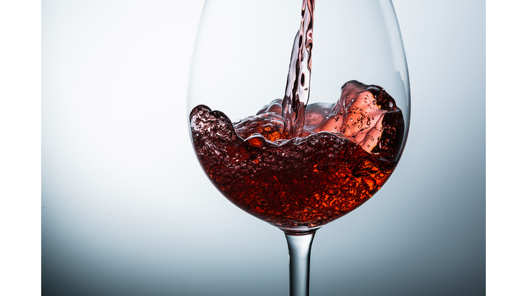 Close-Up Of Red Wine Being Poured In Glass Against White Background