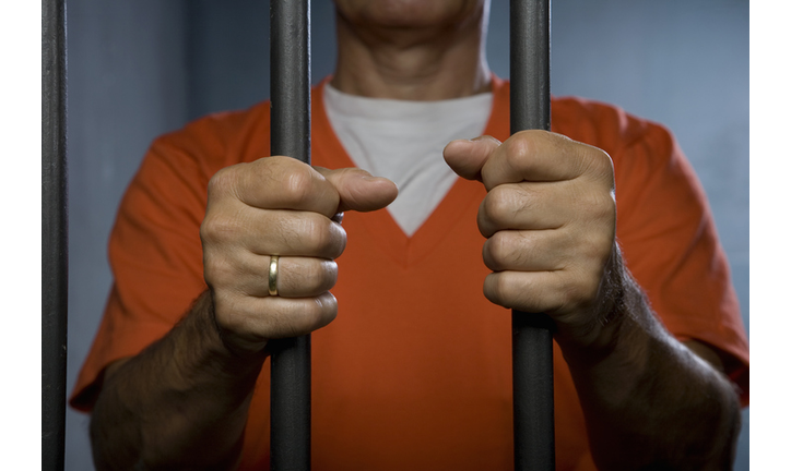 A prisoner standing behind prison bars