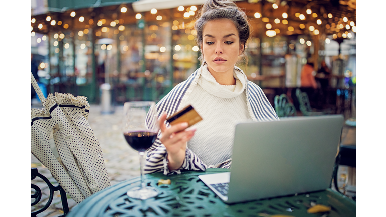 Young woman is shopping online using her credit card and laptop in a rainy day