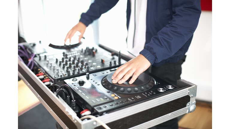 Young male college student spinning DJ turntables in recording studio