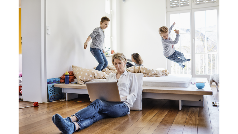 Mother using laptop at home with children romping around in background