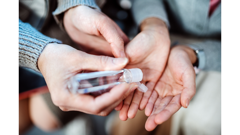 Mom squeezing hand sanitizer onto her littler daughter’s hands