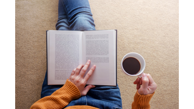 Midsection Of Woman Having Drink While Reading Book On Carpet