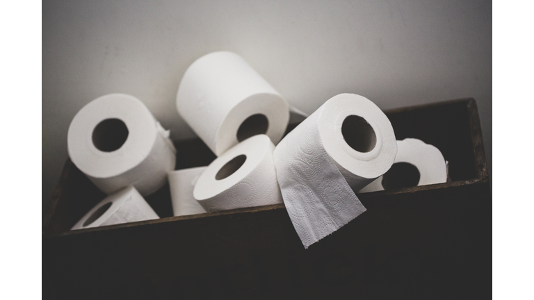 Close up of a pile of toilet paper rolls in a brown wooden crate.