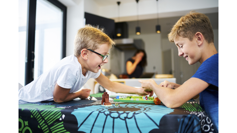 Two brothers laughing playing a board game on the kitchen table