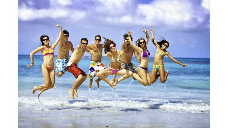 Happy group of young people jumping on a beach party