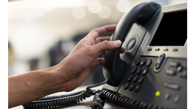 close up employee man hand touching handset of  telephone on desk for contact customer or receiving call , hotline  concept