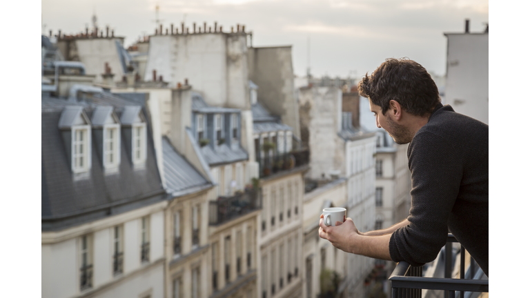 Mid adult man holding coffee cup while leaning on balcony railing  Paris  France