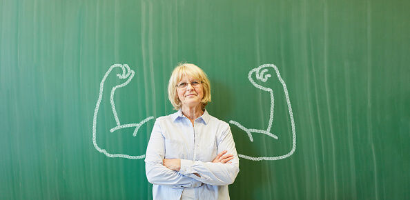 Portrait Of Teacher Standing Against Drawing On Blackboard In Classroom