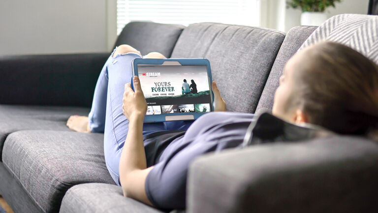 Woman choosing movie from online stream service with tablet. Watching series with on demand video (VOD) website concept. Streaming digital film from site by tv network.
