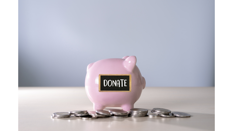 Close-Up Of Piggy Bank With Coins And Donate Text On Table Against Wall