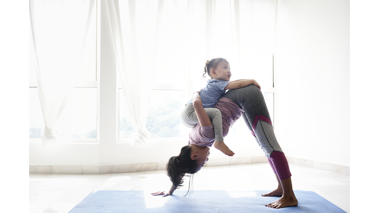 Woman doing yoga with daughter on her back