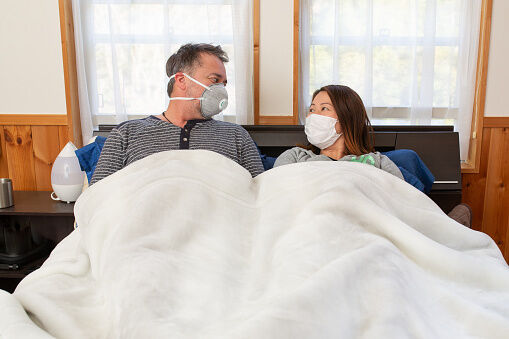 A couple in bed wearing surgical masks