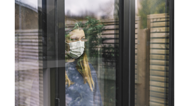 Teenage girl looking through window with mask