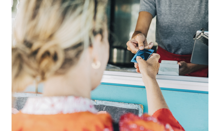 Rear view of female customer giving credit card to owner standing in food truck