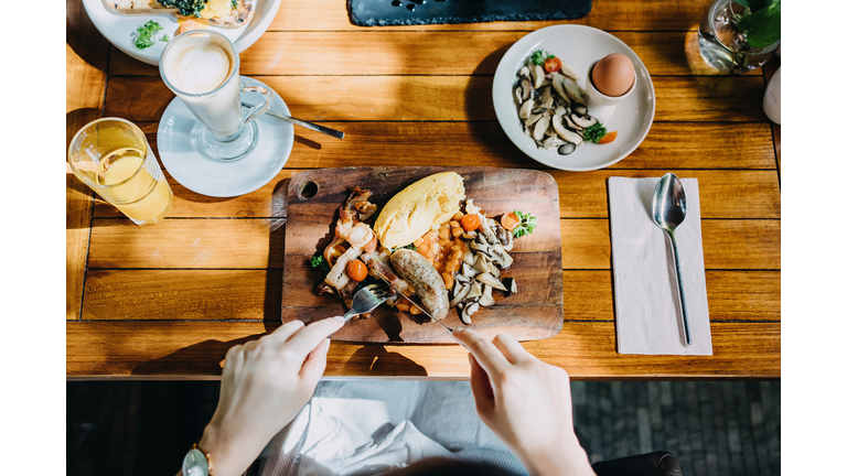 Directly above view of woman having brunch with coffee and orange juice in an outdoor restaurant against beautiful sunlight