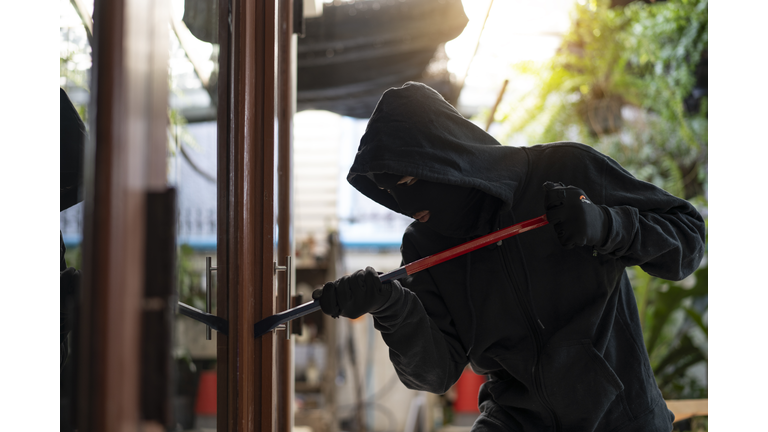 Burglar wearing black clothes and leather coat breaking in a house