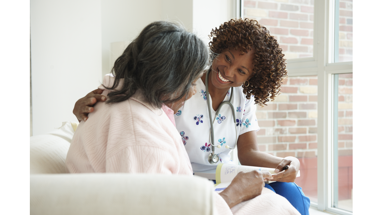 Smiling Nurse Looking At Book With Senior Patient