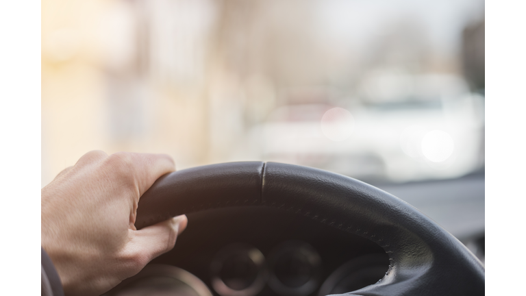 A man's hand grips the steering wheel of his car firmly