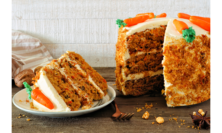 Slice of homemade carrot cake with cream cheese frosting, side view table scene against white wood