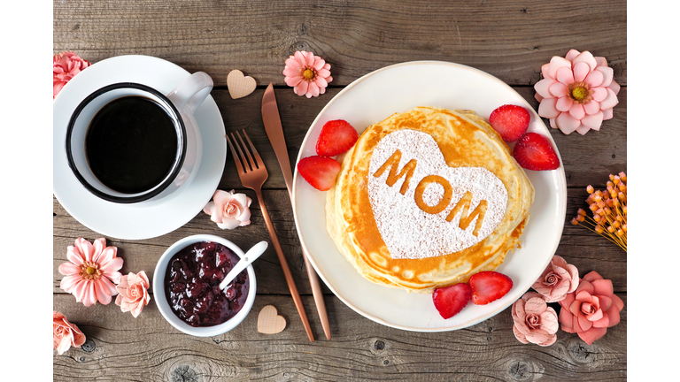 Mothers Day breakfast pancakes with heart shape and MOM letters, overhead view table scene on rustic wood