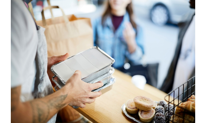 Midsection of salesman holding takeaway packaged food for customers at concession stand