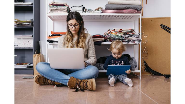 Mother and little daughter sitting on the floor at home using laptop and tablet