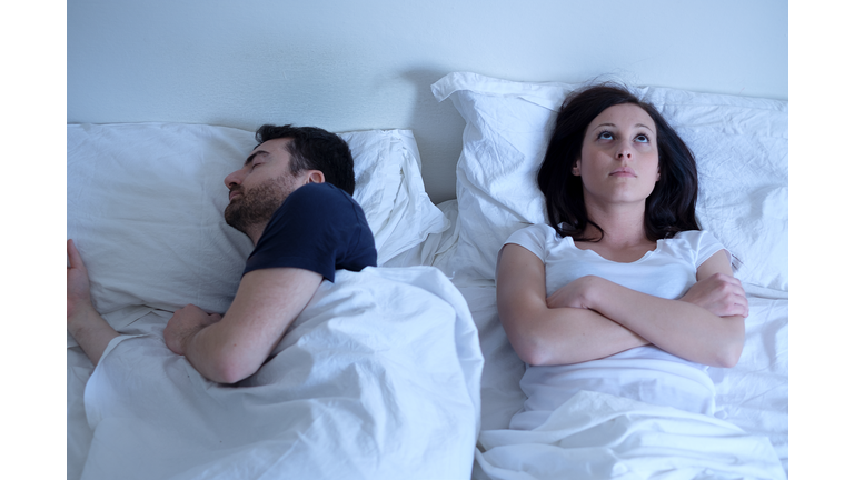 Sad and thoughtful woman awake while husband is sleeping in bed