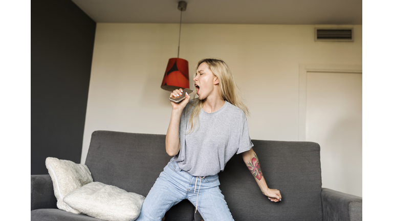 Exuberant young woman on couch with cell phone pretending to sing