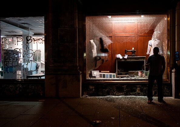People walk past a damaged shop one block from the White House on May 30, 2020 in Washington DC, during a protest over the death of George Floyd.