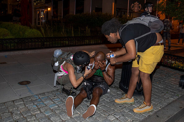 People help clear pepper spray off a mans face as police work to keep demonstrators back during a protest near Lafayette Square Park on May 30, 2020 in Washington, DC.
